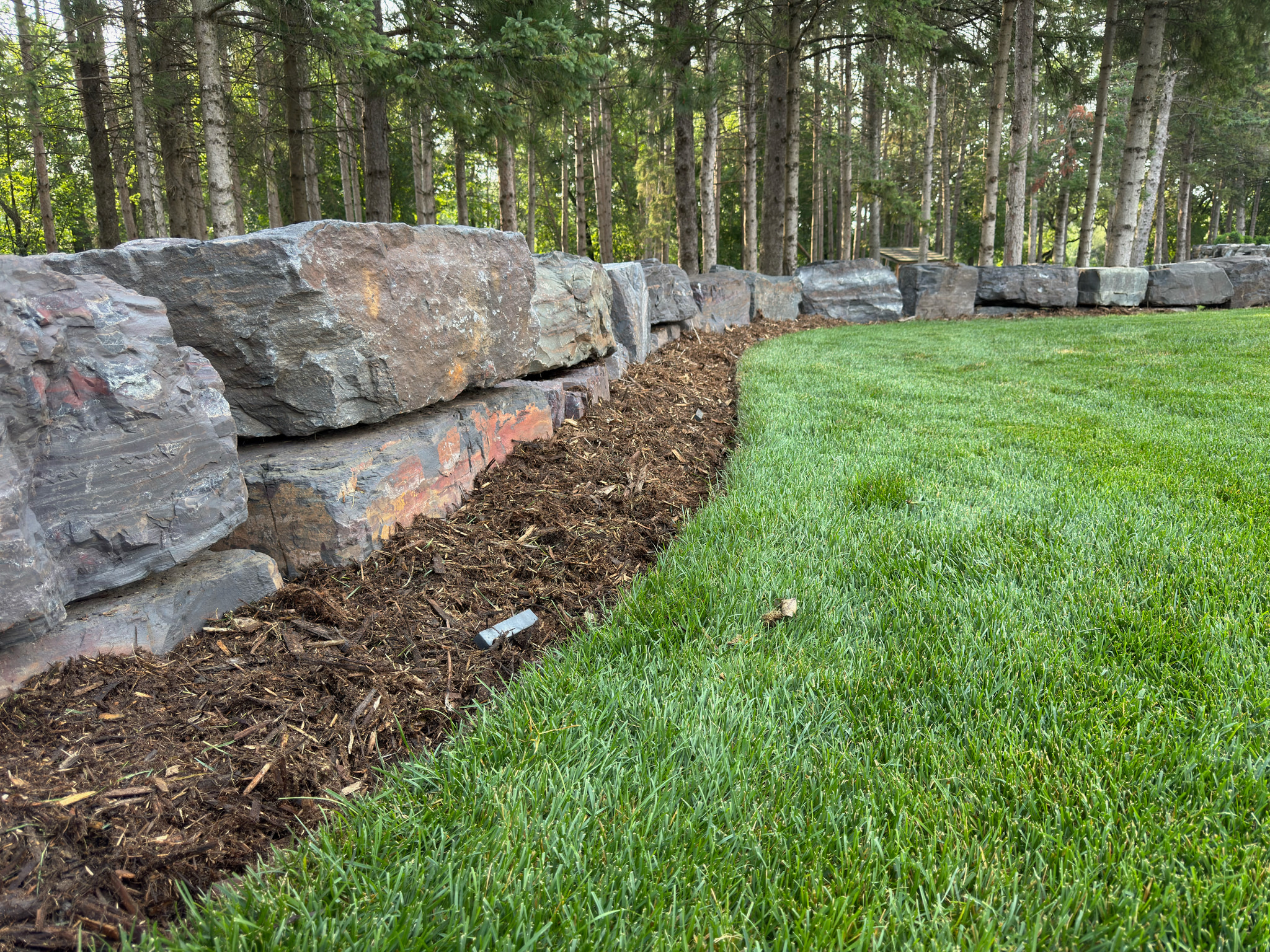 Natural stone boulder wall beside fresh sod and mulch.