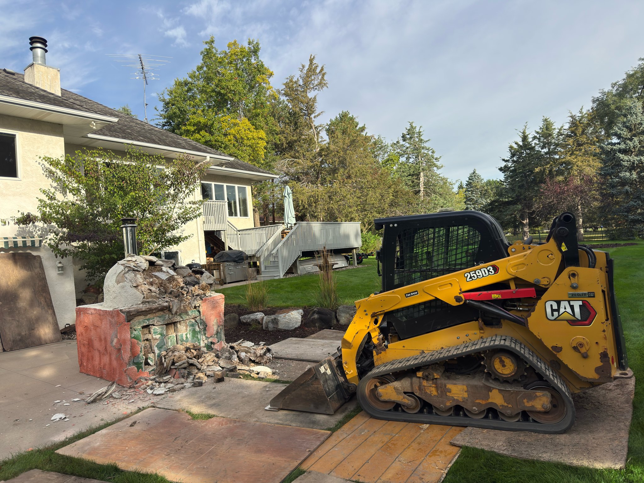 Tracked loader beside a partially demolished outdoor masonry structure on a residential patio.